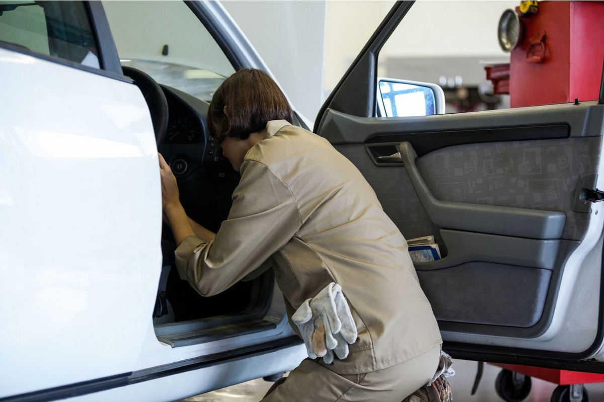 A woman in workwear inspecting a car with an open door