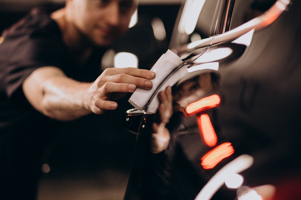 Detailer using a white microfiber cloth to buff the door panel of a glossy black car