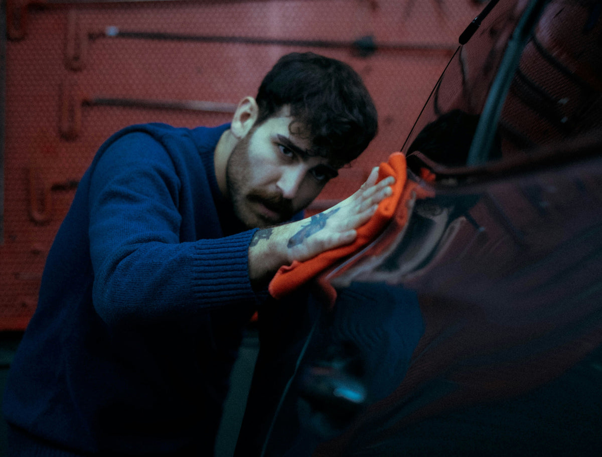 Detailer using an orange microfiber towel to buff a dark car
