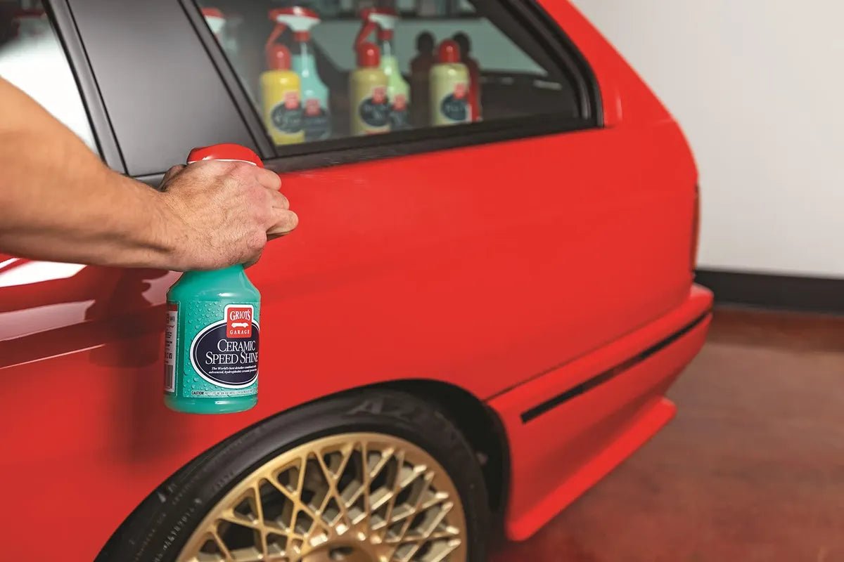 Hand holding a bottle of Griot's Garage Ceramic Speed Shine beside a red car in a garage