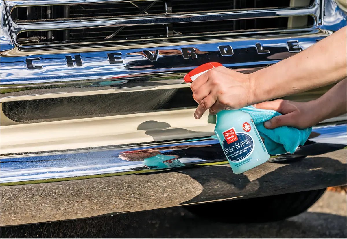 Hand spraying Griot's Garage Speed Shine onto a classic Chevrolet's chrome bumper with a microfiber cloth