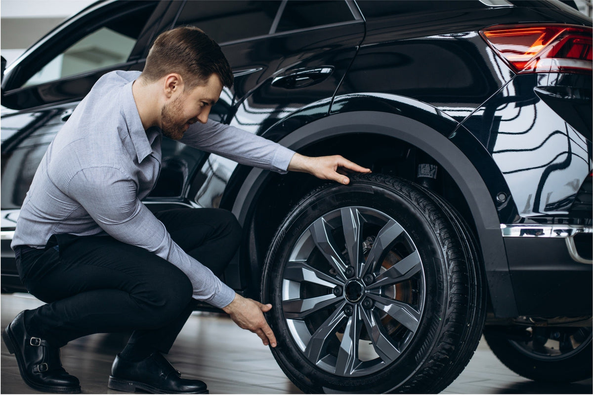 Man crouching beside a black SUV inspecting an alloy matte black wheel