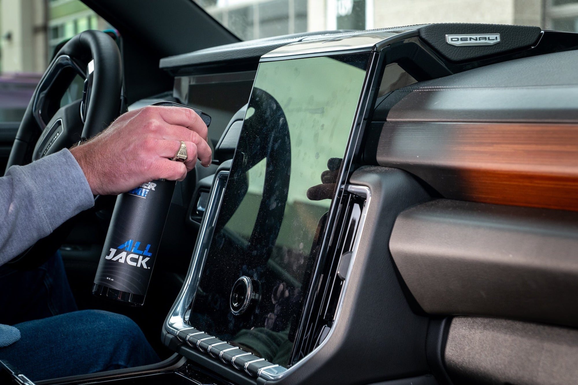 Hand holding an All Jack tumbler inside a GMC Denali vehicle interior with wood trim accents