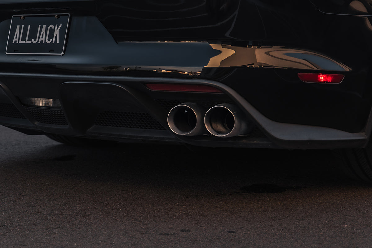 Close-up rear view of a black sports car showing the exhaust system with two polished chrome circular pipes and a custom license plate that reads ALLJACK.